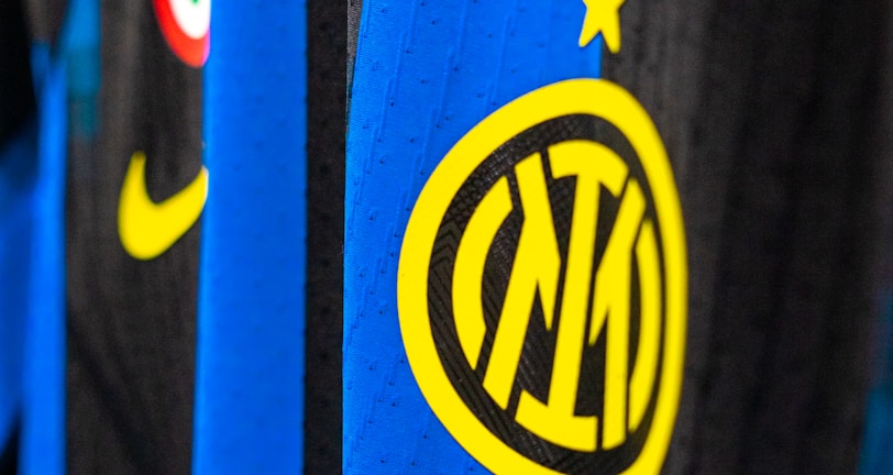 Close-up view of a sports jersey featuring bold vertical stripes in blue and black, adorned with a prominent yellow logo featuring a star on top. Additional elements include a Nike swoosh in yellow, a circular emblem with red, white, and green colors, and a section with black stars on white.